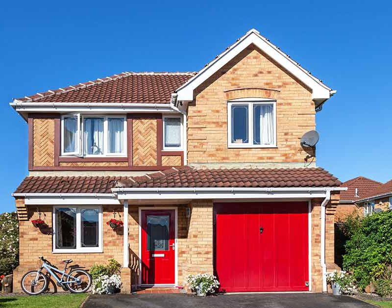 Ein Einfamilienhaus mit Backsteinwand und roter Garagentür vor blauem Himmel - Immobilie finden