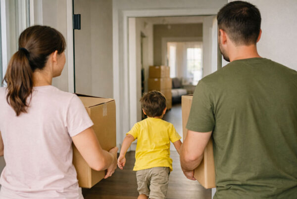 Eine glückliche junge Familie trägt volle Umzugskartons in die neue Wohnung. Sie gehen durch die Haustür ins Haus. Die Familie ist nur von hinten zu sehen. Das Kind rennt spielerisch vor den Eltern ins Haus. Förderung Familien